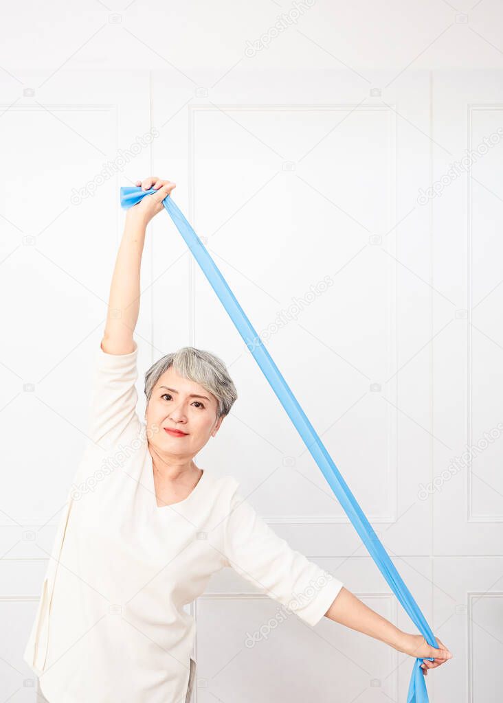 Senior asian woman doing exercises with resistance band at home.