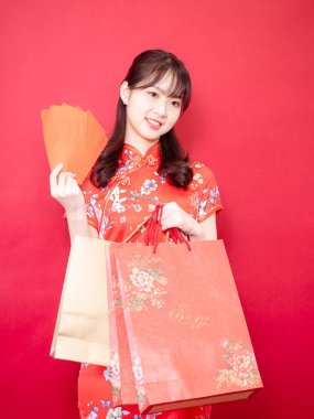 Güzel, genç Asyalı bir kadın geleneksel Cheongsam Qipao elbisesi giyiyor kırmızı zarflı ve hediye çantaları Çin 'in yeni yıl konseptinde kırmızı arka planda..