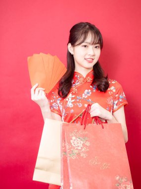 Güzel, genç Asyalı bir kadın geleneksel Cheongsam Qipao elbisesi giyiyor kırmızı zarflı ve hediye çantaları Çin 'in yeni yıl konseptinde kırmızı arka planda..