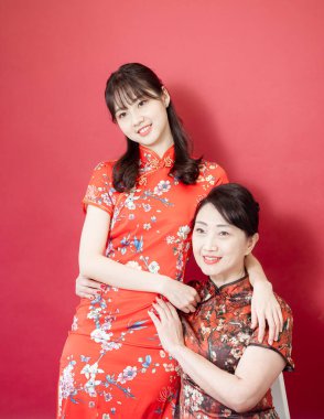 Olgun Asyalı anne kırmızı arka planda Asyalı kızıyla kucaklaşıyor. (İkisi de geleneksel Cheongsam Qipao giyiyor)).