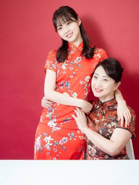 Olgun Asyalı anne kırmızı arka planda Asyalı kızıyla kucaklaşıyor. (İkisi de geleneksel Cheongsam Qipao giyiyor)).