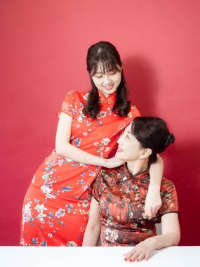 Olgun Asyalı anne kırmızı arka planda Asyalı kızıyla kucaklaşıyor. (İkisi de geleneksel Cheongsam Qipao giyiyor)).