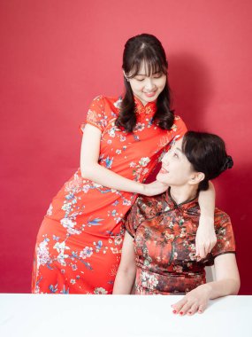 Olgun Asyalı anne kırmızı arka planda Asyalı kızıyla kucaklaşıyor. (İkisi de geleneksel Cheongsam Qipao giyiyor)).
