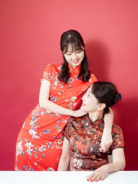 Olgun Asyalı anne kırmızı arka planda Asyalı kızıyla kucaklaşıyor. (İkisi de geleneksel Cheongsam Qipao giyiyor)).