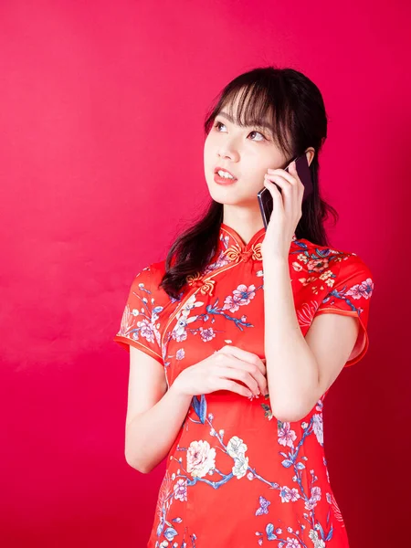 中国の伝統的なチョンサムQipaoドレスを身に着けている若いアジアの女性の肖像画赤の背景にスマートフォンを使用して — ストック写真