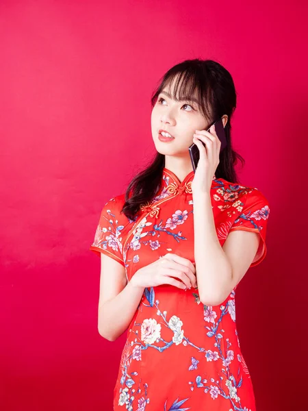 中国の伝統的なチョンサムQipaoドレスを身に着けている若いアジアの女性の肖像画赤の背景にスマートフォンを使用して — ストック写真