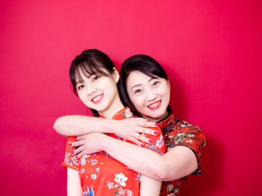 Geleneksel Cheongsam Qipao giyen bir anne ve kızın portresi ve kırmızı arka planda izole edilmiş gülümseme..