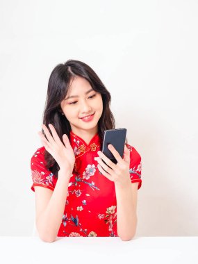 Geleneksel Cheongsam Qipao elbisesi içinde gülümseyen Asyalı genç kadın video görüşmesi için telefon uygulaması kullanıyor..