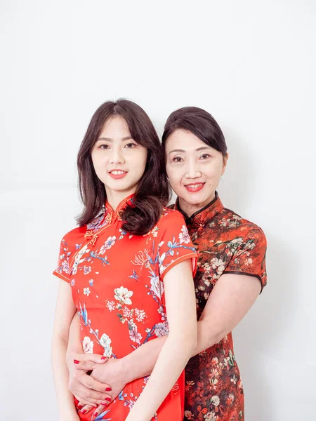 Beyaz arka planda Asyalı kızıyla kucaklaşan olgun Asyalı annenin portresi.).