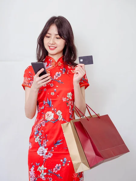 ショッピングバッグ スマートフォン 白い背景に隔離されたクレジットカードを示す伝統的なChongsam Qipaoドレスを身に着けている若いアジアの女性の肖像 — ストック写真