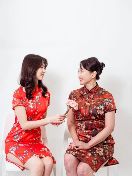 Portrait of asian young daughter and mother wearing traditional cheongsam qipao and smiling with flowers carnation in hands isolated on white background.