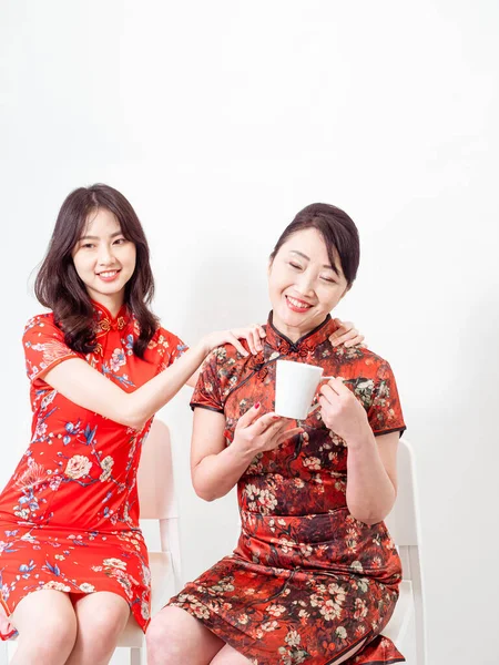 Asyalı genç kızın beyaz arka planda rahatlamak için annesine masaj yaptığı portre (her ikisi de geleneksel Cheongsam Qipao elbisesi giyiyor)).