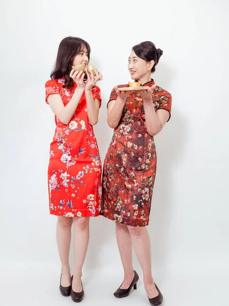 İkisi de geleneksel Cheongsam Qipao elbisesi giyen Asyalı kadınların portresi Çin 'in yeni yılını beyaz arka planda kutlamak için altın külçelerini gösteriyor..