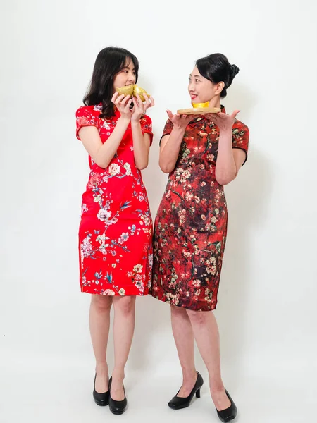 İkisi de geleneksel Cheongsam Qipao elbisesi giyen Asyalı kadınların portresi Çin 'in yeni yılını beyaz arka planda kutlamak için altın külçelerini gösteriyor..