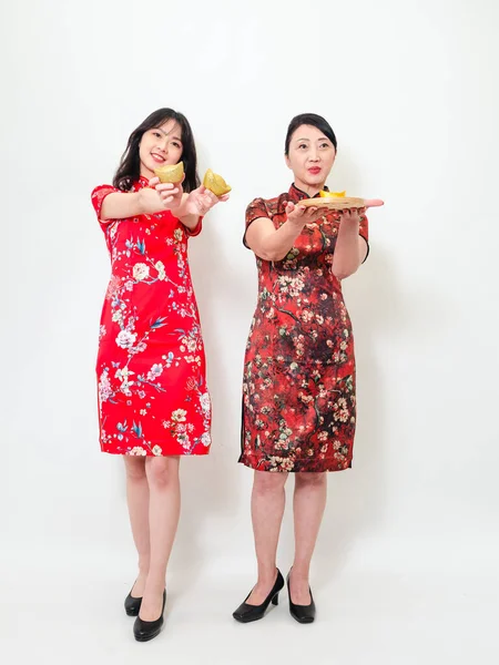 İkisi de geleneksel Cheongsam Qipao elbisesi giyen Asyalı kadınların portresi Çin 'in yeni yılını beyaz arka planda kutlamak için altın külçelerini gösteriyor..