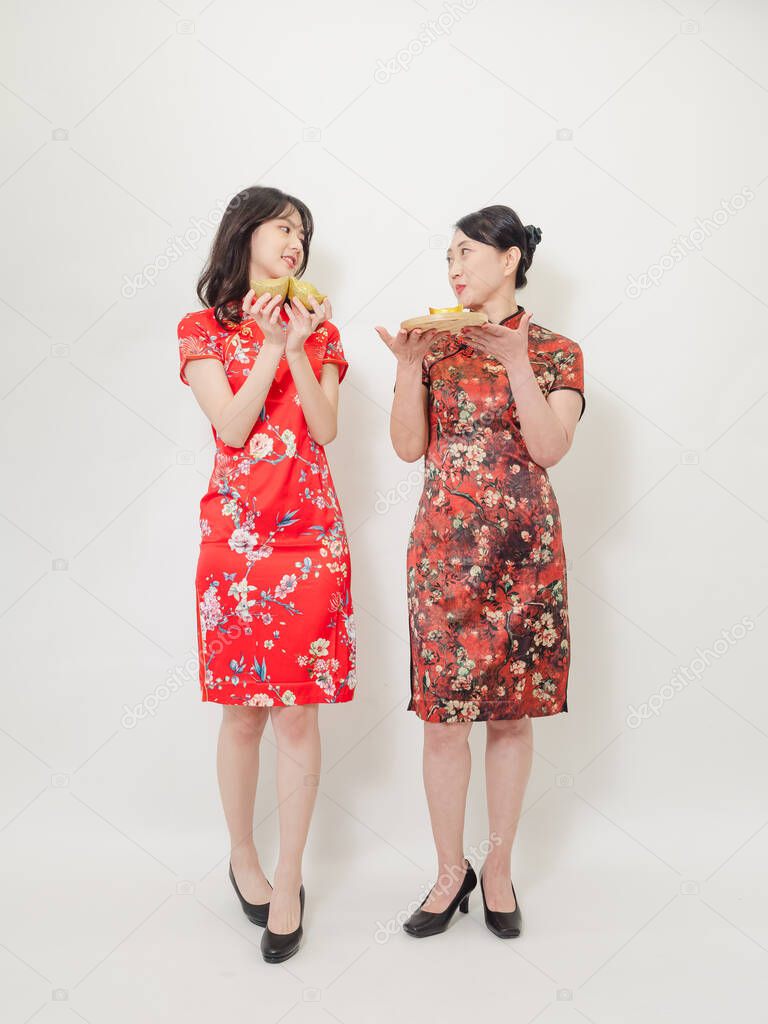 Portrait of asian women both wearing traditional cheongsam qipao dress showing Gold ingot for celebrating chinese new year on white background.