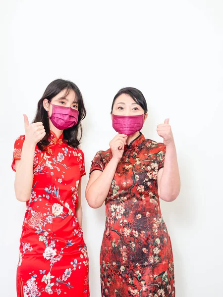 Portrait of asian women both wearing traditional cheongsam qipao dress wearing facemask during isolated on white background.