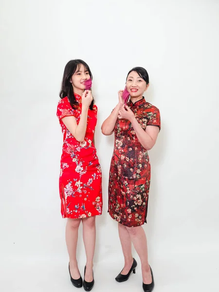 Portrait of asian women both wearing traditional cheongsam qipao dress wearing facemask during isolated on white background.