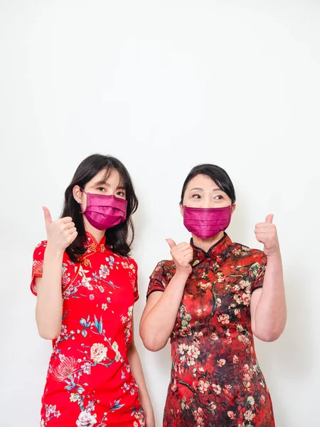 Portrait of asian women both wearing traditional cheongsam qipao dress wearing facemask during isolated on white background.