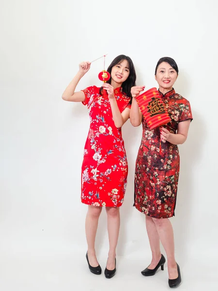 Portrait of young asian woman and elder woman both wearing traditional cheongsam qipao dress hold red paper lantern with word meaning good fortune and treasure on white background.