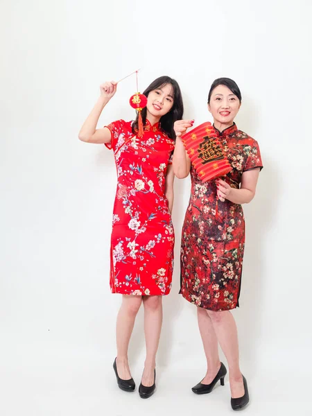 Portrait of young asian woman and elder woman both wearing traditional cheongsam qipao dress hold red paper lantern with word meaning good fortune and treasure on white background.