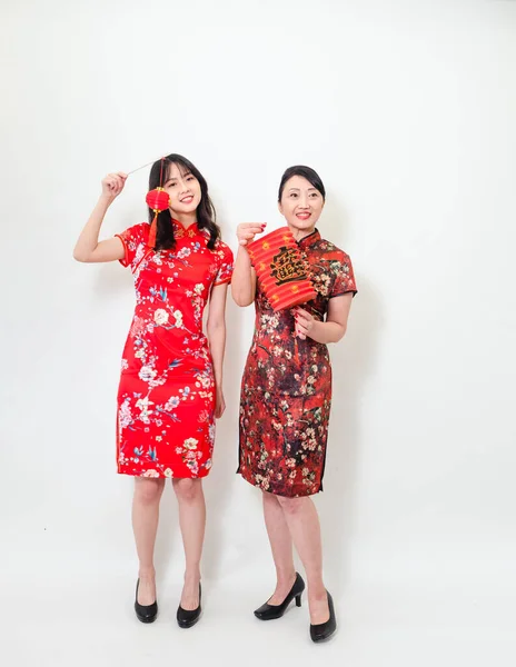 Portrait of young asian woman and elder woman both wearing traditional cheongsam qipao dress hold red paper lantern with word meaning good fortune and treasure on white background.