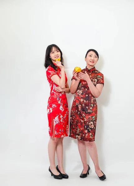 Portrait of asian young woman and elder woman both wearing traditional cheongsam qipao dress showing Gold ingot and pig meaning 