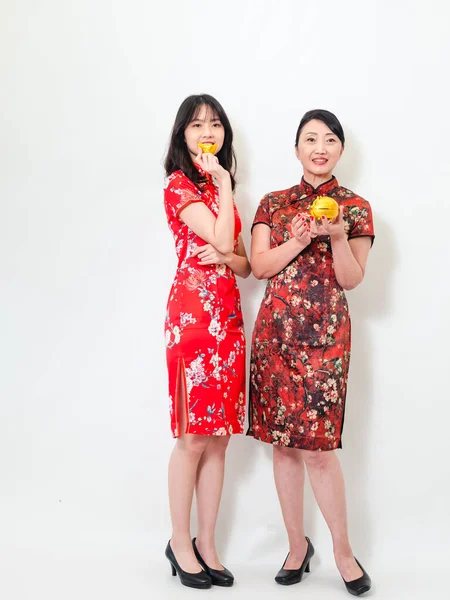 Portrait of asian young woman and elder woman both wearing traditional cheongsam qipao dress showing Gold ingot and pig meaning 