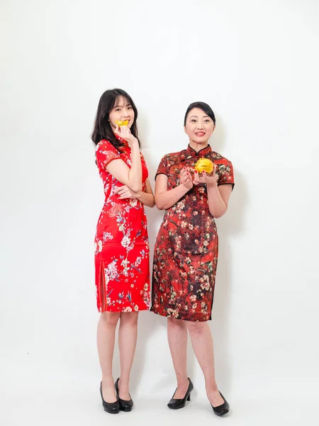 Portrait of asian young woman and elder woman both wearing traditional cheongsam qipao dress showing Gold ingot and pig meaning \