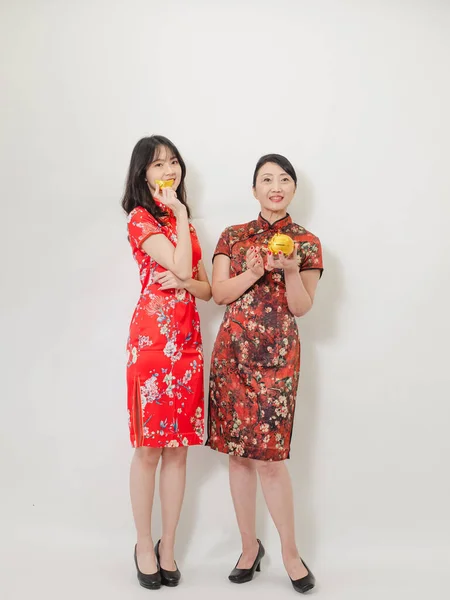 Portrait of asian young woman and elder woman both wearing traditional cheongsam qipao dress showing Gold ingot and pig meaning \