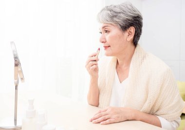 Olgun Asyalı kadın portresi. 60 'larında aynaya bakarak ruj sürüyor..