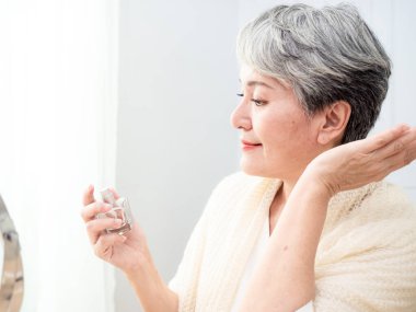 Olgun Asyalı kadın portresi 60 'lı yaşlarda parfüm sıkar..