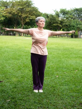 Portrait of happy senior adult elderly asia woman smiling standing and stretch her arms relax and enjoy with nature fresh air in the park.