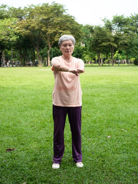Portrait of happy senior adult elderly asia woman smiling standing and stretch her arms relax and enjoy with nature fresh air in the park.