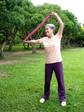 Yetişkin Asyalı kadın portresi. Spor giysileri giyiyor. Parkta sağlıklı olmak için lastik bantla egzersiz yapıyor..