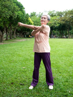 Yaşlı, yaşlı Asyalı bir kadının portresi. 60 'lı yaşlarda gülümseyen ve kollarını uzatan. Rahatlayıp parkta temiz havanın tadını çıkaran..