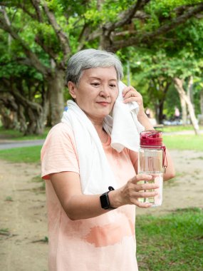 60 'ların yaşlı, yaşlı Asyalı kadının portresi ayakta gülümseyen, elinde su şişesi tutan ve parkta temiz havanın tadını çıkaran bir kadın..