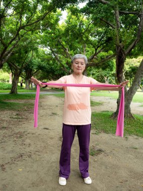 Yetişkin Asyalı kadın portresi. Spor giysileri giyiyor. Parkta sağlıklı olmak için lastik bantla egzersiz yapıyor..