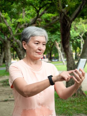 Yaşlı, yaşlı Asyalı bir kadının portresi. 60 'lı yaşlarda, gülümsüyor ve parkta akıllı telefon tutuyor..