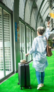 Yaşlı, yaşlı Asyalı bir kadının portresi. 60 'larında bavul çantasıyla gülümseyen ve seyahat konsepti için güdümlü bayrak direği tutan..