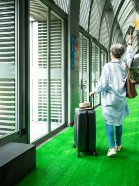 Yaşlı, yaşlı Asyalı bir kadının portresi. 60 'larında bavul çantasıyla gülümseyen ve seyahat konsepti için güdümlü bayrak direği tutan..