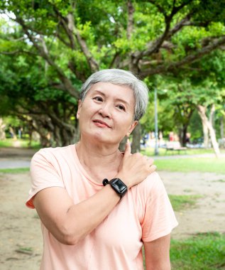 Portrait of mature asian woman 60s with shoulder pain at park outdoor.