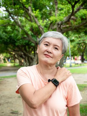 Portrait of mature asian woman 60s with shoulder pain at park outdoor.