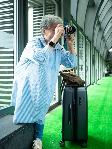 Mutlu yetişkin yaşlı Asyalı kadının portresi. 60 'lı yaşlarda seyahat konsepti için fotoğraf makinesiyle fotoğraf çekiyor..