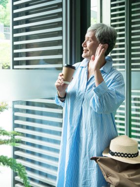 Yaşlı mutlu bir kadının portresi. 60 'lı yaşlarda. Elinde kağıt bardak, seyahat konsepti için kahve içiyor..