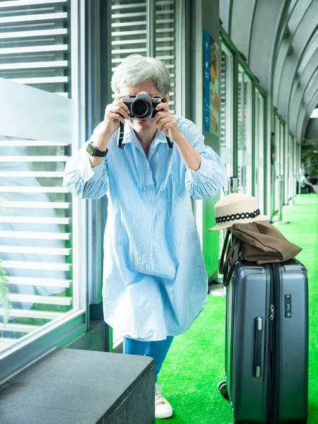 Mutlu yetişkin yaşlı Asyalı kadının portresi. 60 'lı yaşlarda seyahat konsepti için fotoğraf makinesiyle fotoğraf çekiyor..