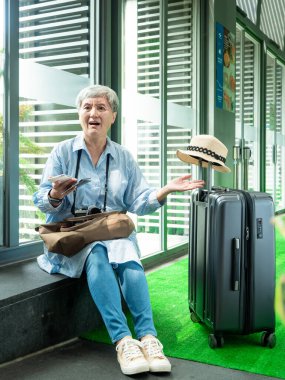 Yaşlı, yaşlı Asyalı bir kadının portresi. 60 'larında gülümseyen, bavul çantasıyla oturan ve seyahat konsepti için pasaport taşıyan..