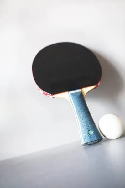 Gri arka planda raket ve ping pong topu.
