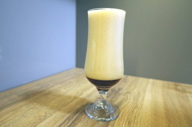 Tahta bir masanın üstünde bira için uzun bir bardak. Köpüklü koyu