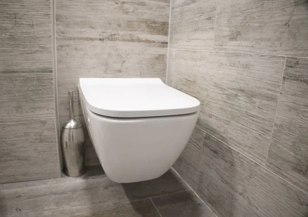 Duvara asılmış beyaz tuvalet. Gri fayanslar, banyo.